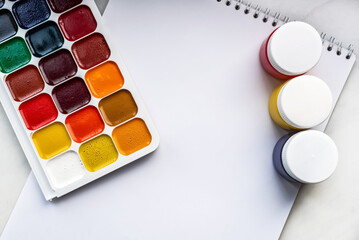 Colorful watercolor or acrylic paints and pencils on a white sheet of paper on a white background. Design studio table top view. Space for text.
