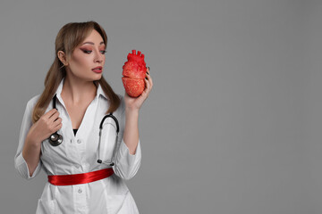 Woman in scary nurse costume with heart model on light grey background, space for text. Halloween...
