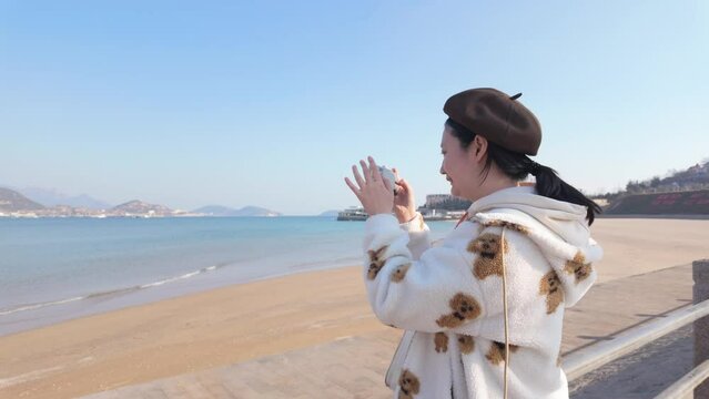 An Asian girl happily taking photos by the seaside
