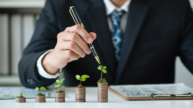 Businessman with coin stack at his office as sustainable money growth investment or eco-subsidize. Green corporate promot and invest in environmental awareness. Gyre