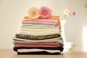 Stack of clean clothes and flowers on wooden table