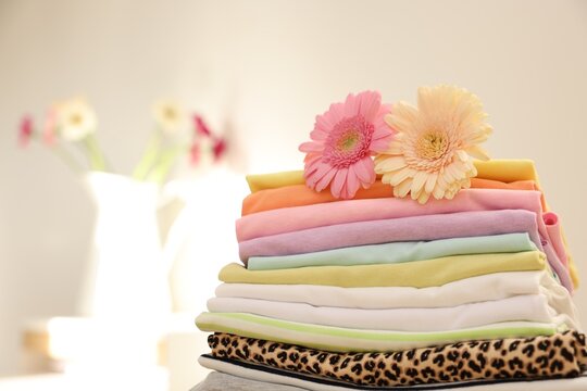 Stack of clean clothes and flowers on blurred background. Space for text