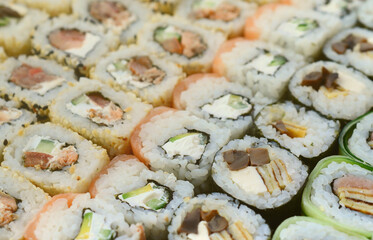 Close-up of a lot of sushi rolls with different fillings lie on a wooden surface. Macro shot of cooked classic Japanese food with a copy space.