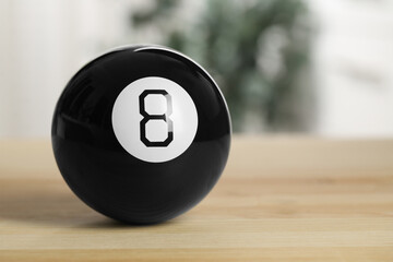 Magic eight ball with on wooden table, closeup. Space for text