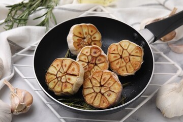 Frying pan with fried garlic and rosemary on table, closeup