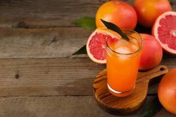 Tasty grapefruit drink with ice in glass and fresh fruits on wooden table. Space for text