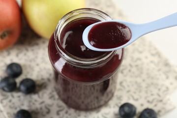 Eating baby food with spoon at white table, closeup