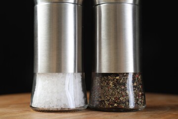 Salt and pepper shakers on wooden table against black background, closeup