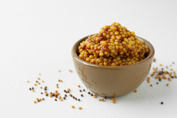 Fresh whole grain mustard in bowl and dry seeds on white table. Space for text