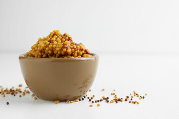Fresh whole grain mustard in bowl and dry seeds on white table. Space for text