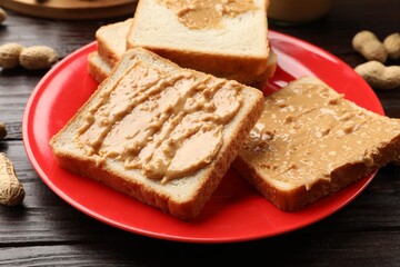 Delicious toasts with peanut butter on dark wooden table, closeup