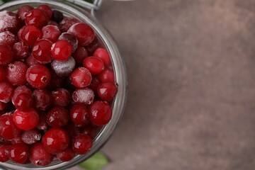 Frozen red cranberries in glass jar on brown textured table, top view. Space for text