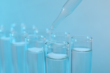 Laboratory analysis. Dripping reagent into test tube on light blue background, closeup