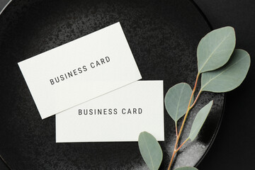 Business cards and eucalyptus branch on black plate, top view