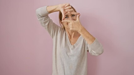 Joyful middle aged blonde woman, beautifully making a frame shape with her hands and fingers over a pink isolated background. a lively symbol of photography creativity and happy vision.