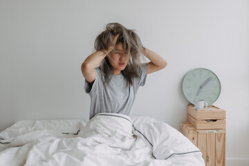 Asian woman just wake up by the clock at 7 AM on the bed in the morning. - obrazy, fototapety, plakaty