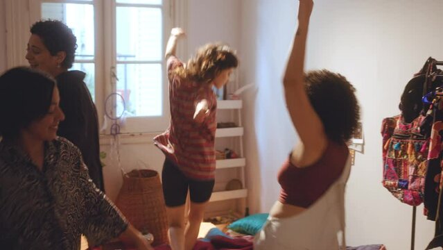 Company of four energetic girls jumping, laughing and dancing with excitement on bed at home party