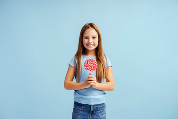 Smiling little girl wearing casual clothes, holding lolly pop, looking at camera