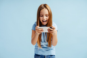 Portrait of happy little girl wearing casual clothes holding mobile phone, playing game