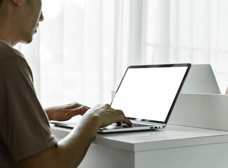 Man's hands using laptop with blank screen on white table at home or office.
