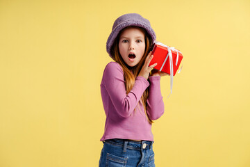 Portrait of interested little girl holding red gift box, feeling curious