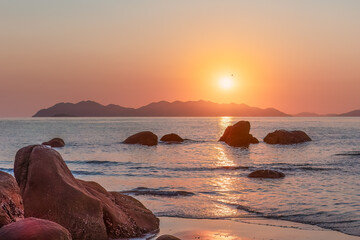 Sunrise over islands and rocks with reflection on the water at Rose Bay in Bowen in the Whitsunday region of tropical Queensland, Australia.