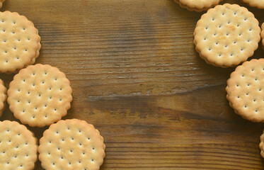 A round sandwich cookie with coconut filling lies in large quantities on a brown wooden surface. Photo of edible treats on a wooden background with copy space