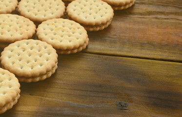 A round sandwich cookie with coconut filling lies in large quantities on a brown wooden surface. Photo of edible treats on a wooden background with copy space