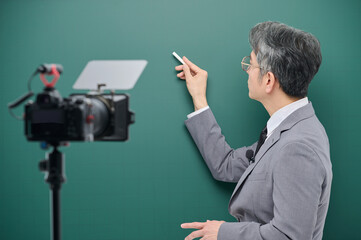 A middle-aged man is wearing a suit and giving a lecture in front of the camera pointing to the blackboard.