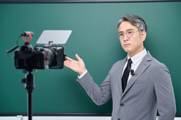 A middle-aged man is wearing a suit and giving a lecture in front of the camera pointing to the blackboard.