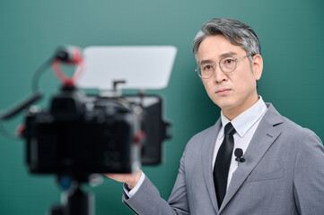 A middle-aged man is wearing a suit and giving a lecture in front of the camera pointing to the...