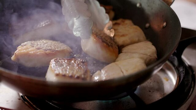油が跳ねる熱いフライパンで魚を焼きソテーし焼き目をつける料理人　調理・食事・レストラン・シェフ