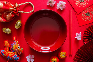 Red plate with chopstick on red cloth background with ingots(word mean wealth), red bag, dragon pendant and red envelope packet or ang bao(word mean blessing) for Chinese new year dinner concept.