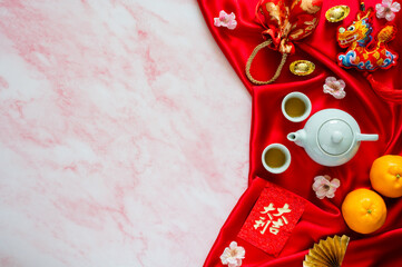 Tea set on red cloth background with red envelope packets or ang bao(word mean auspice), red bag, ingots(word mean wealth), hanging pendant dragon and oranges on marble table.