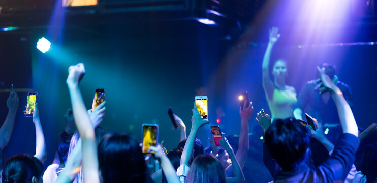 music concert live on stage. Audience Captures the show with smartphone. diverse young people dancing in night club. Nightlife and disco dance party concept. Fun music festival