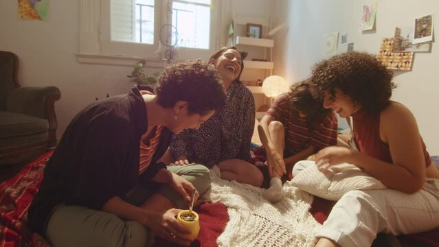 Group of joyous girls resting on bed in cozy living room and laughing together on a funny joke during home party. Whip zoom shot