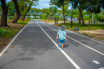 Little boy walking on city park pathway green tree forest