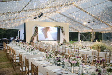 
Long table setting with beautiful flower arrangements for intimate wedding or party-outdoors family gathering on sunny day under transparent tent
