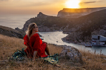 Woman sunset sea mountains. Happy woman siting with her back on the sunset in nature summer posing...