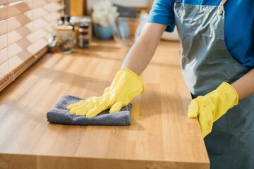 Housewife or maid in modern kitchen wipes dining table surface. Using professional cleaning...