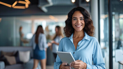 Fototapeta premium A business woman wearing a blue shirt stands in her office with his tablet.