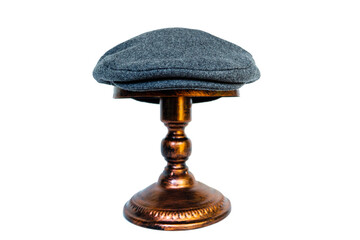 Detail of a scaly hat or flat cap or made of tweed herringbone mounted on a bronze mannequin head on a white background. Catalog photo of a classic dark gray hat on an elegant bronze mannequin - obrazy, fototapety, plakaty