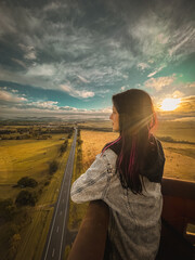 Photo of the young attractive woman standing in the hot air ballooning basket. Beautiful landscape...