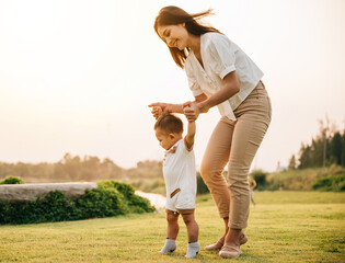 A beautiful Asian family enjoying a sunny day in the park as they teach their baby to take his...