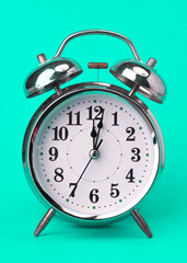 Classic vintage alarm clock isolated on green background. Retro alarm clock with twelve o'clock.