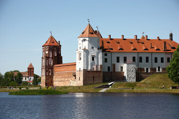 Obraz premium Sunny spring day. In the distance behind the lake ancient Mir Castle Complex is visible. Around fresh greens of leaves and grass.