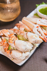 Steamed crab meat and legs on a white plate with seafood dipping sauce.