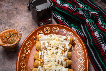 Fried potato tacos with cream and cheese in a Mexican mud dish. Tacos dorados, Mexican food.