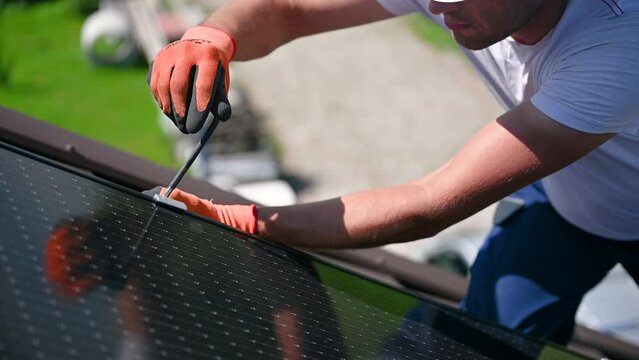 Worker building photovoltaic solar panel system on rooftop of house. Close up of man engineer in gloves installing solar module with help of hex key outdoors. Renewable energy generation concept.