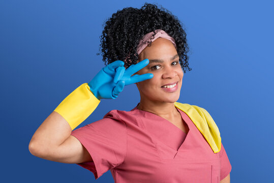 Freundliche, weibliche Reinigungskraft mit Afro in Arbeitskleidung und Gummihandschuhen beim Fr&uuml;hjahrsputz, freigestellt auf blauem Hintergrund 